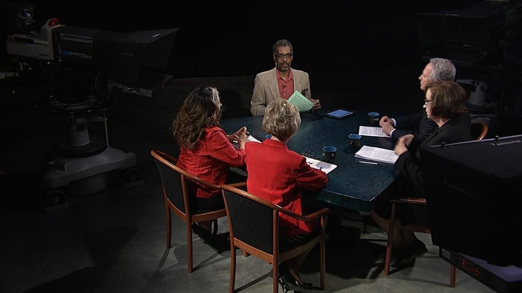 A group of people sitting at a table in front of a camera.