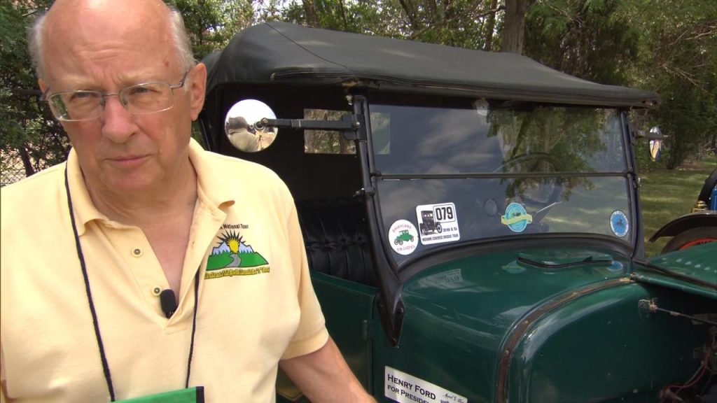 An older man standing next to a green car.