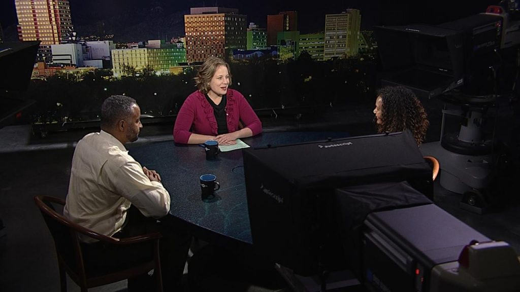 Three people sitting around a table in a television studio.