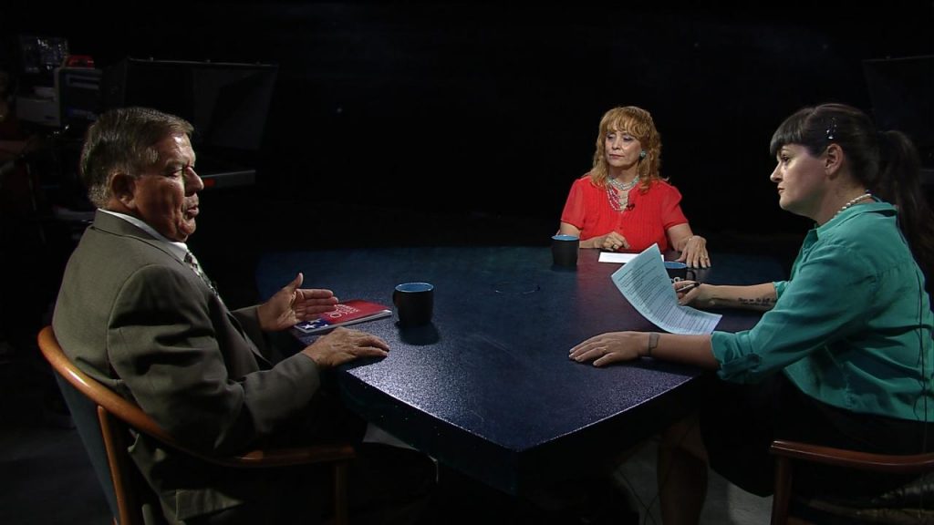 Three people sitting at a table talking to each other.