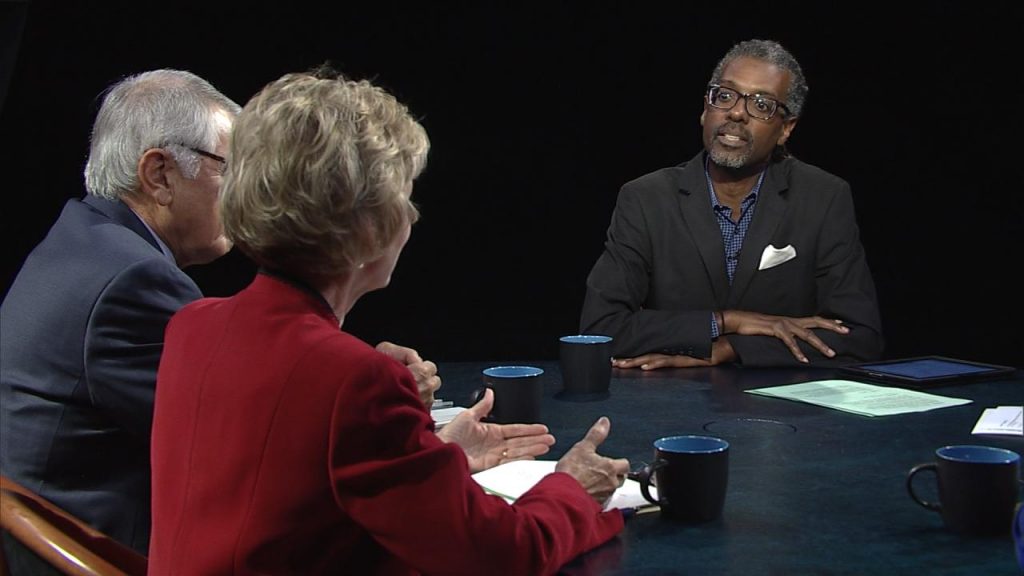 Three people sitting at a table talking to each other.