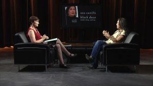 Two women sitting in chairs talking on a stage.