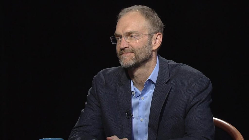 A man in glasses sitting in a chair.