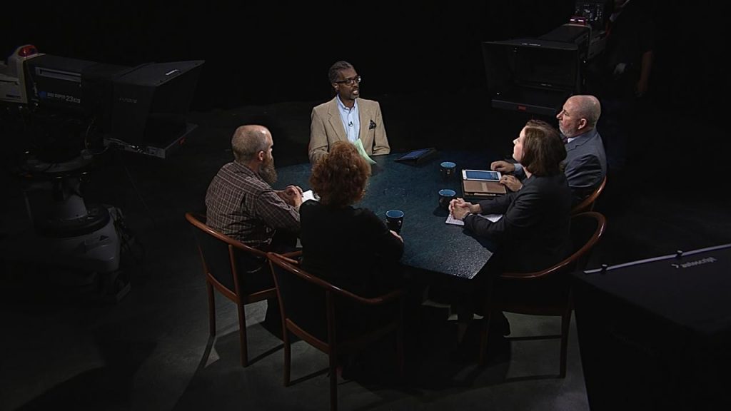 A group of people sitting around a table in front of a camera.