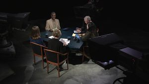 A group of people sitting around a table in front of a camera.