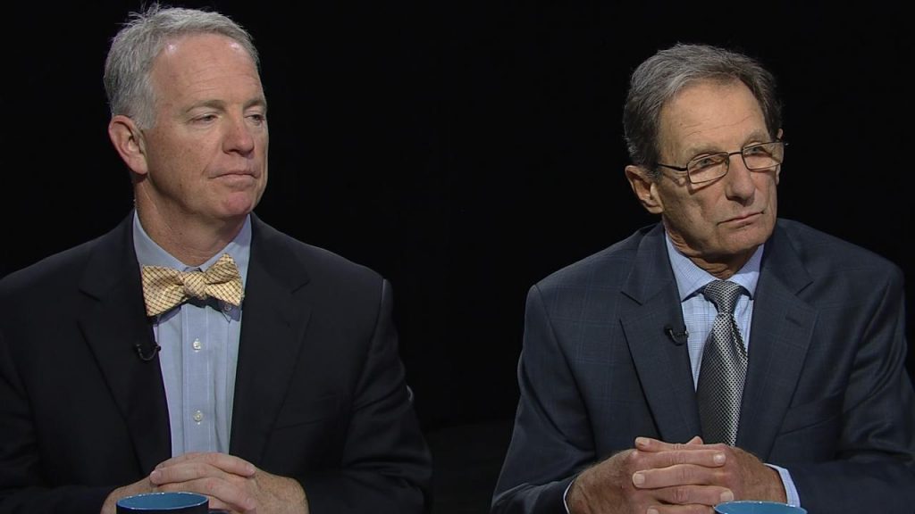 Two men in suits sitting next to each other.