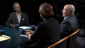 Three people sitting at a table talking to each other.