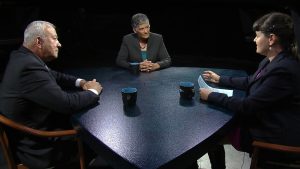 Three people sitting at a table talking to each other.