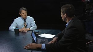 Two men sitting at a table talking to each other.