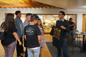 A group of people standing around a room with a t - shirt.