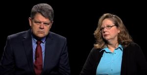 A man and woman sitting in front of a black background.