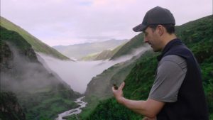 A man standing in front of a valley with a waterfall.