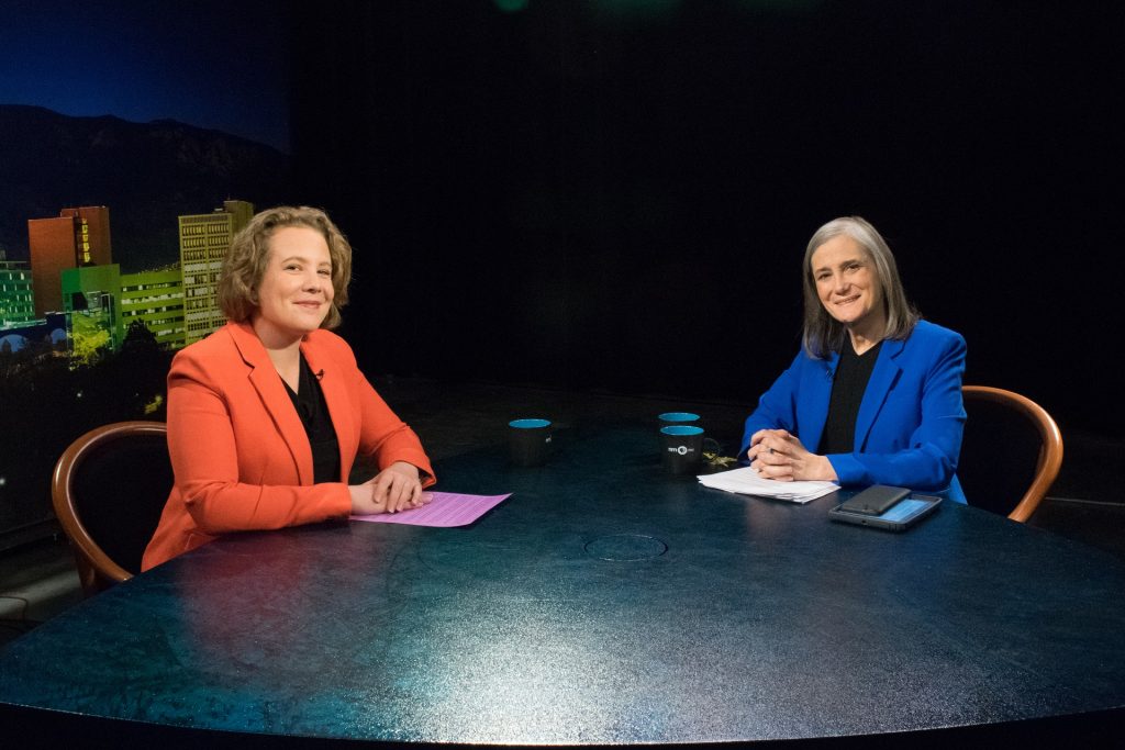 Two women sitting at a table in front of a city.