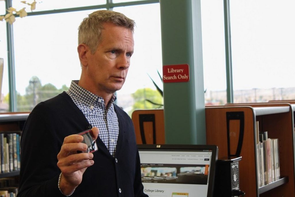 A man standing in a library holding a cell phone.