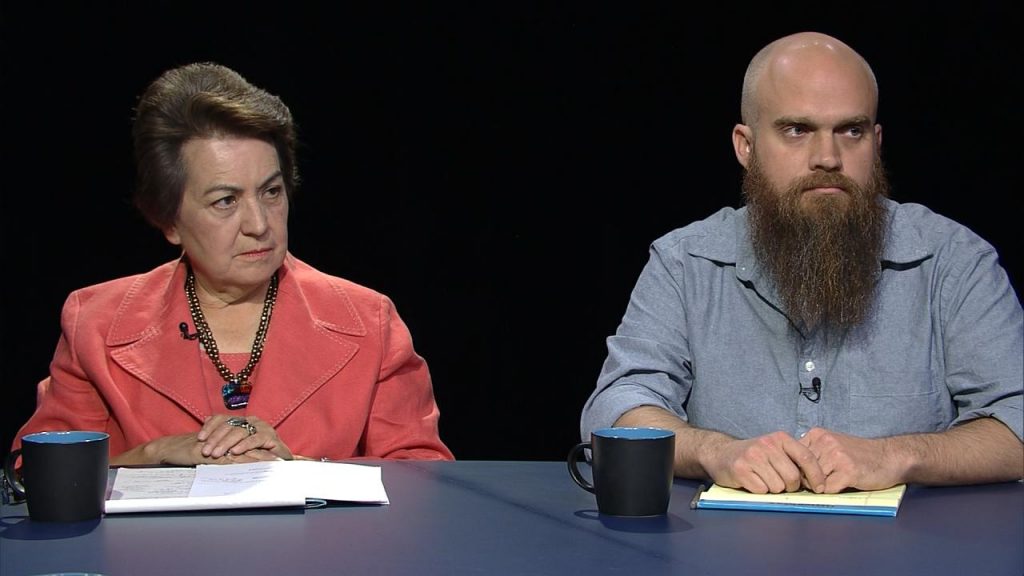 Two people sitting at a table with papers and a beard.
