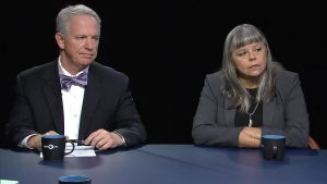 Two people sitting at a table in front of mugs.