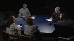 A group of people sitting around a table in front of a camera.