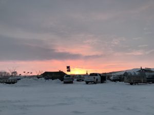 The sun is setting over a parking lot in the snow.