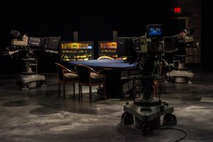 A table and chairs in a dark room with two televisions.