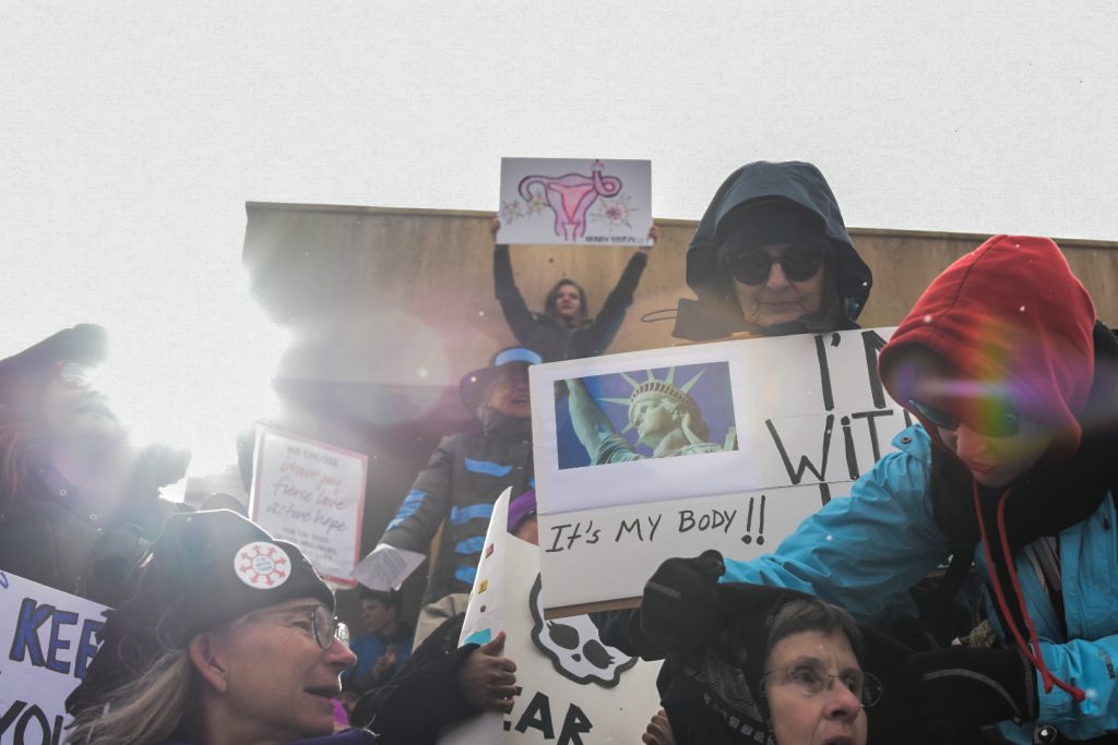 Rally participants standing on the Civic Plaza fountain brace for winter weather conditions during the Abq Women’s Rally, Saturday, Jan. 21st, 2017, in Albuquerque, NM. The rally in Albuquerque was a single gathering held in concert with hundreds of rallies and marches spread across the country and around the world. The sister rally in Civic Plaza was “to show solidarity across the nation and at home,” according to social media accounts affiliated with the rally. (Kevin Maestas / @ DailyLobo) 