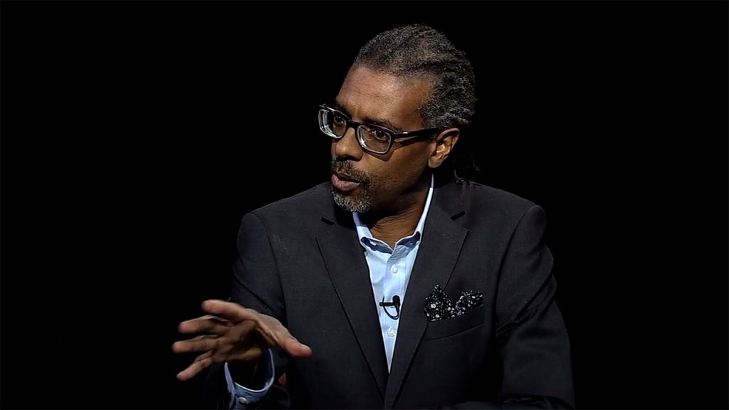 A man in a suit and tie is talking on a black background.