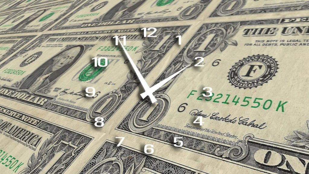 A clock is sitting on top of a stack of dollar bills.
