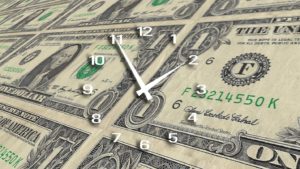 A clock is sitting on top of a stack of dollar bills.