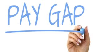 A hand writing the word pay gap on a white board.