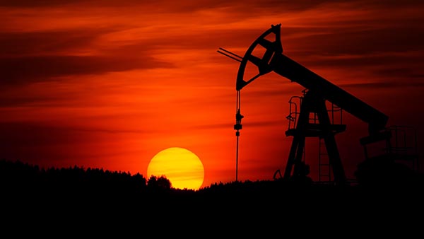 An oil pumpjack at work outdoors as the sun rises in the background.