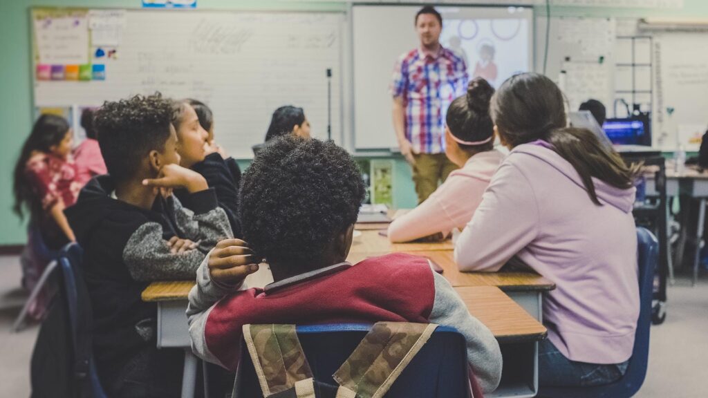 Students in a classroom listen to a speaker at the front of the room.