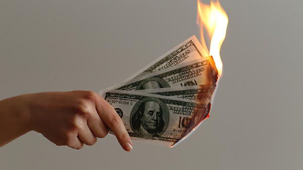 A hand holds four $100 dollar bills on fire.
