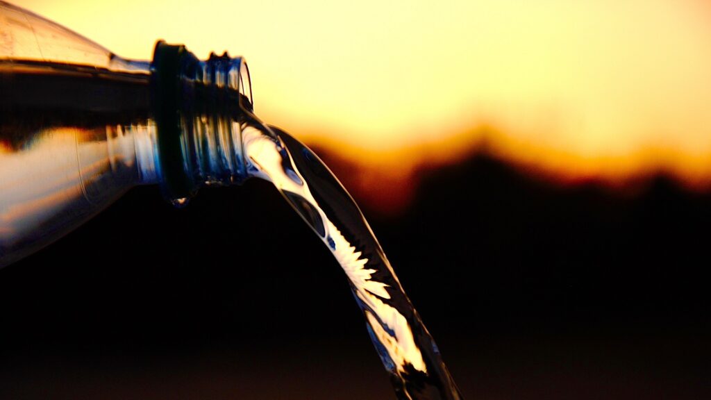 A bottle pours out a stream of water in front of a yellow-orange sky.