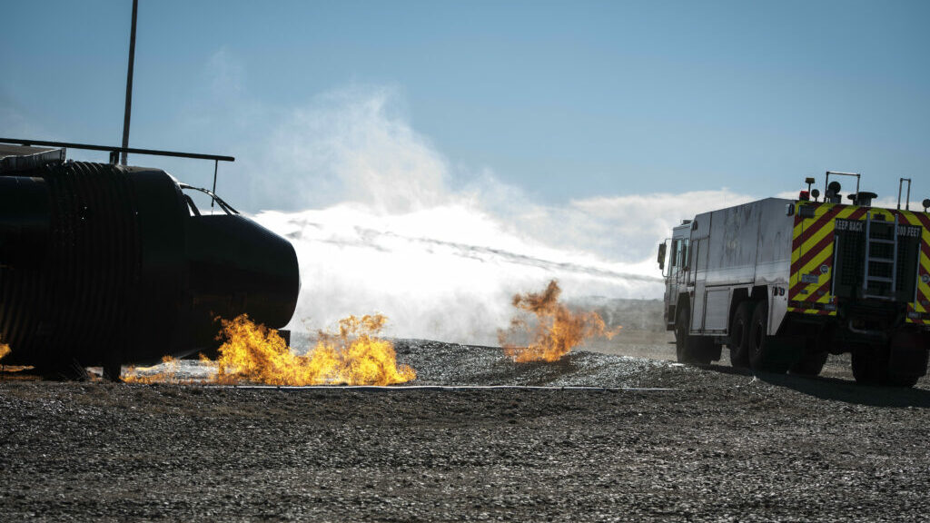 A firetruck shoots water at a fire in the desert.