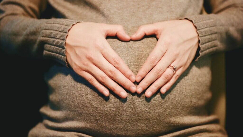 Close-up of hands placed on a pregnant stomach, the fingers creating the shape of a heart.