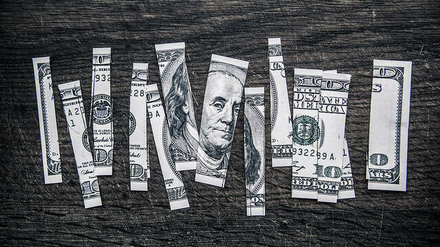 A cut-up $100 dollar bill on a grey wooden surface.