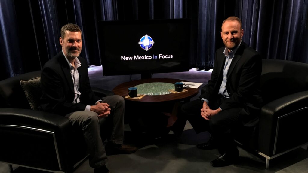 Two people sitting in leather chairs pose towards camera, hands clasped.