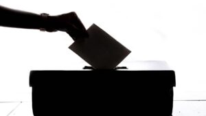 Silhouette of a hand placing a ballot in a box.