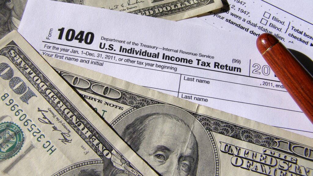 A 1040 tax return with $100 dollar bills lying on top of it.