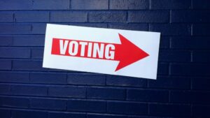 A sign with an arrow and label reading "VOTING" on a blue brick wall.