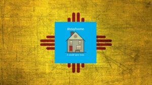 Composite of illustration of a house with label "#stayhome it could save lives", with the New Mexico flag in the background.