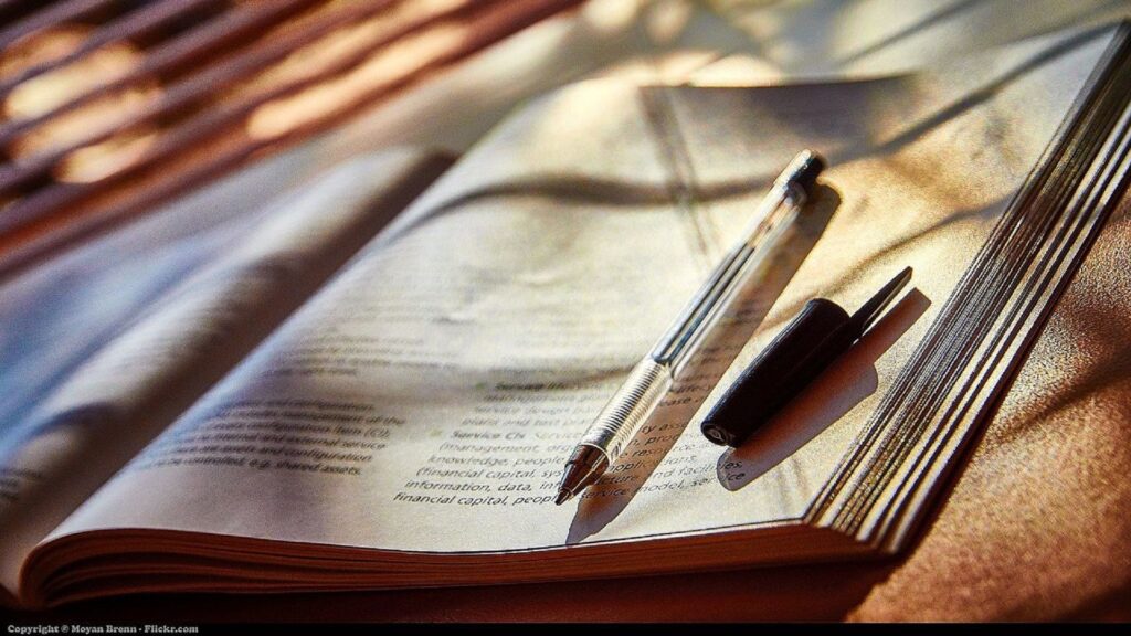 A pen sits on top of a magazine as light seeps through a window.