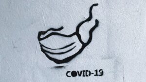 A spray-painted illustration of a facemask, featuring a caption reading "COVID-19".