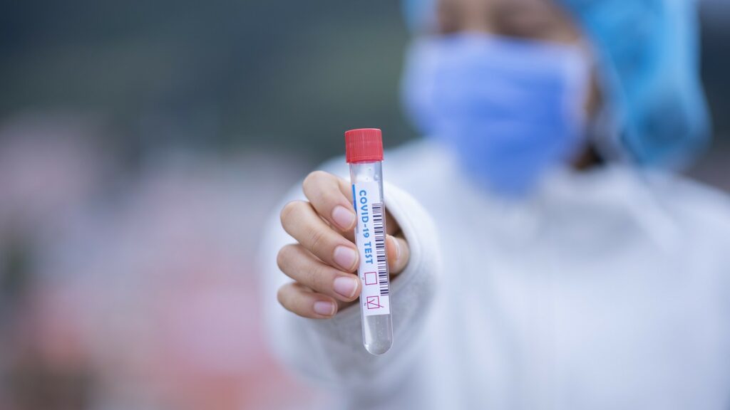 A nurse holds up a vial reading "COVID-19 TEST".