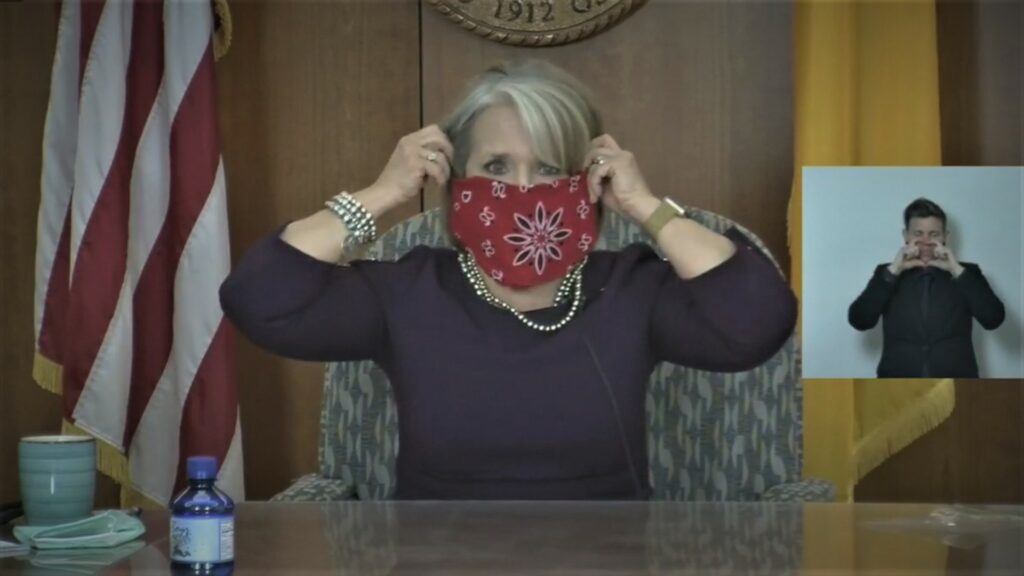 Governor Michelle Lujan Grisham places a bandana over her mouth in lieu of a facemask.