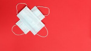 Two surgical facemasks on top of each other creating an X shape, on a red backdrop.