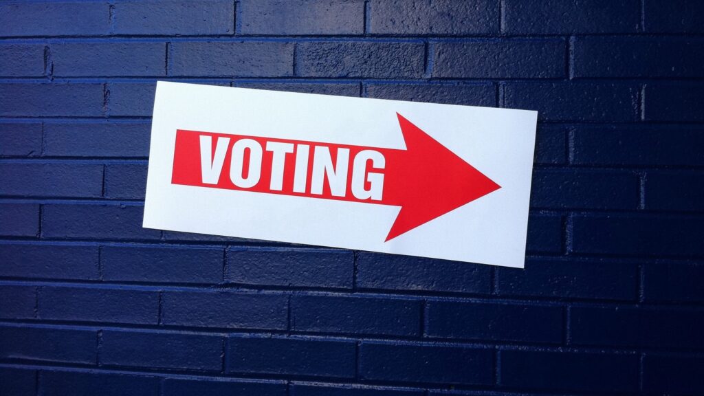 A red arrow reading "VOTING" on top of a blue-painted brick wall.