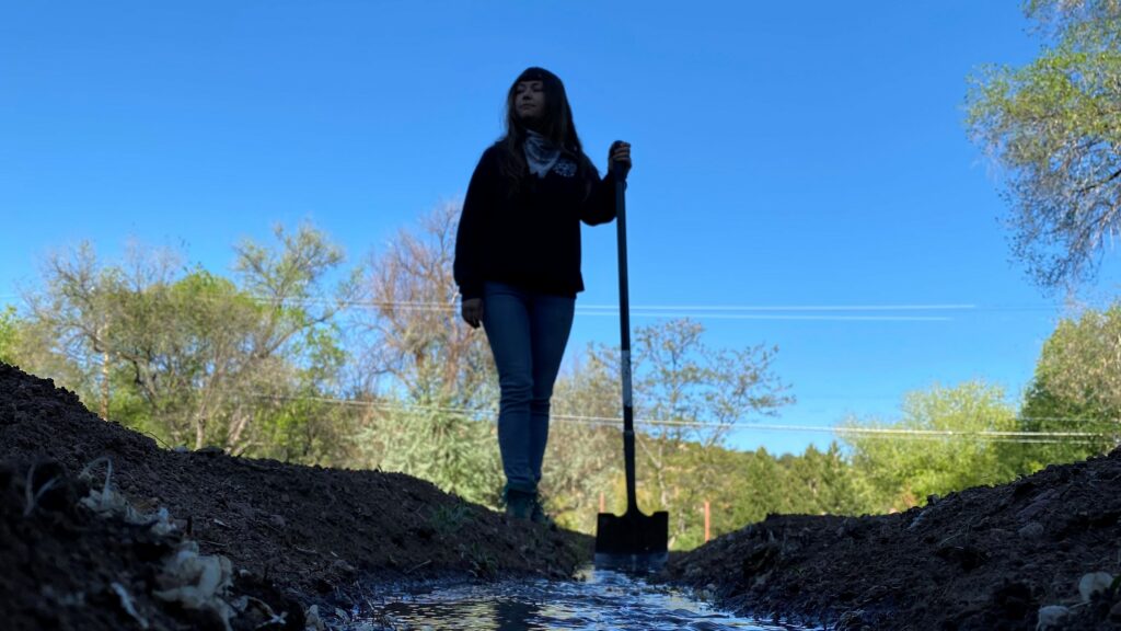A person stands in dirt, holding a shovel in their hand.