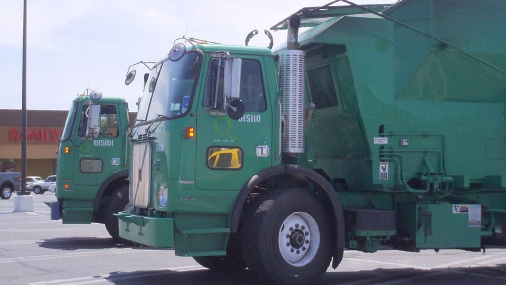 Two green trask trucks in a parking lot.