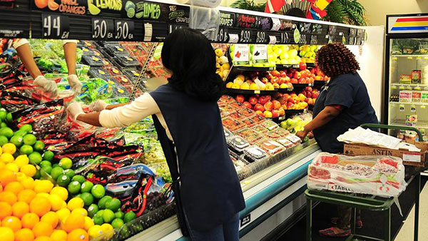 Two people place produce on shelves in a grocery store.