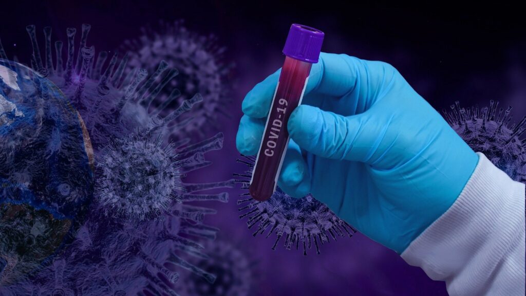 Composite of a gloved hand holding a vial reading "COVID-19", with close-ups of coronaviruses in the background.